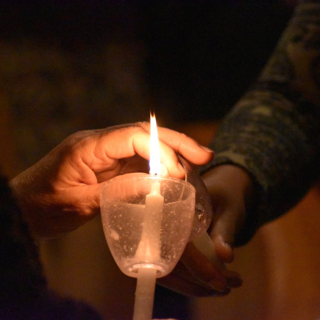 Two hands holding taper candles, transferring the flame from one candle to the other. 