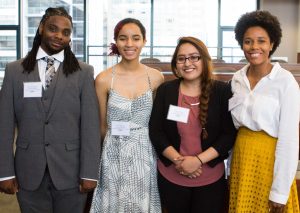 Four young people of color, wearing suits and dresses, smile for the camera.