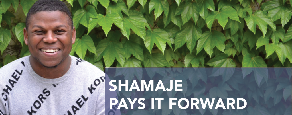 Shamaje, a young Black man, smiles while posing in front of a leafy backdrop. He is wearing a gray Michael Kors sweater. White text reads: Shamaje pays it forward.