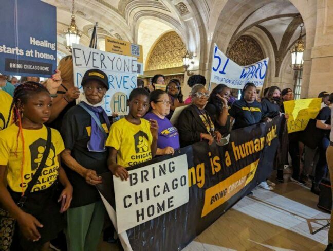 Bring Chicago Home supporters rally with banners and signs inside of City Hall.