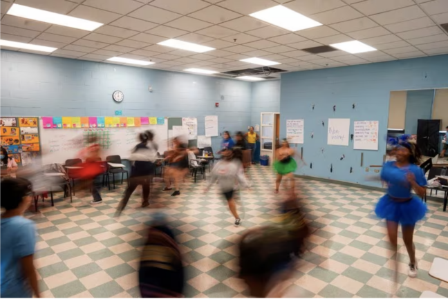 A group of children run around a classroom in Chicago.